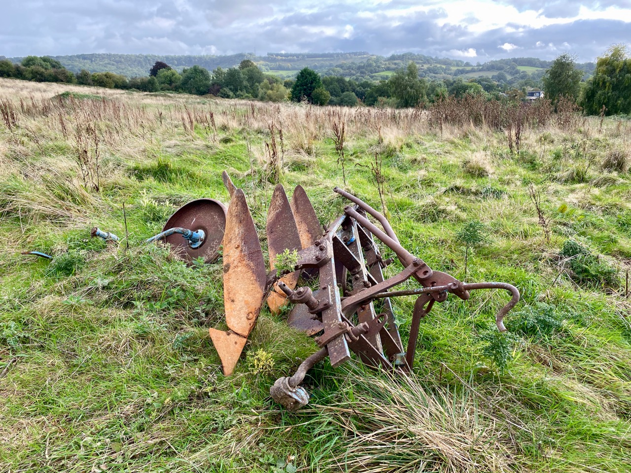 Rusty abandoned farm equipment in a field with a backdrop of hills