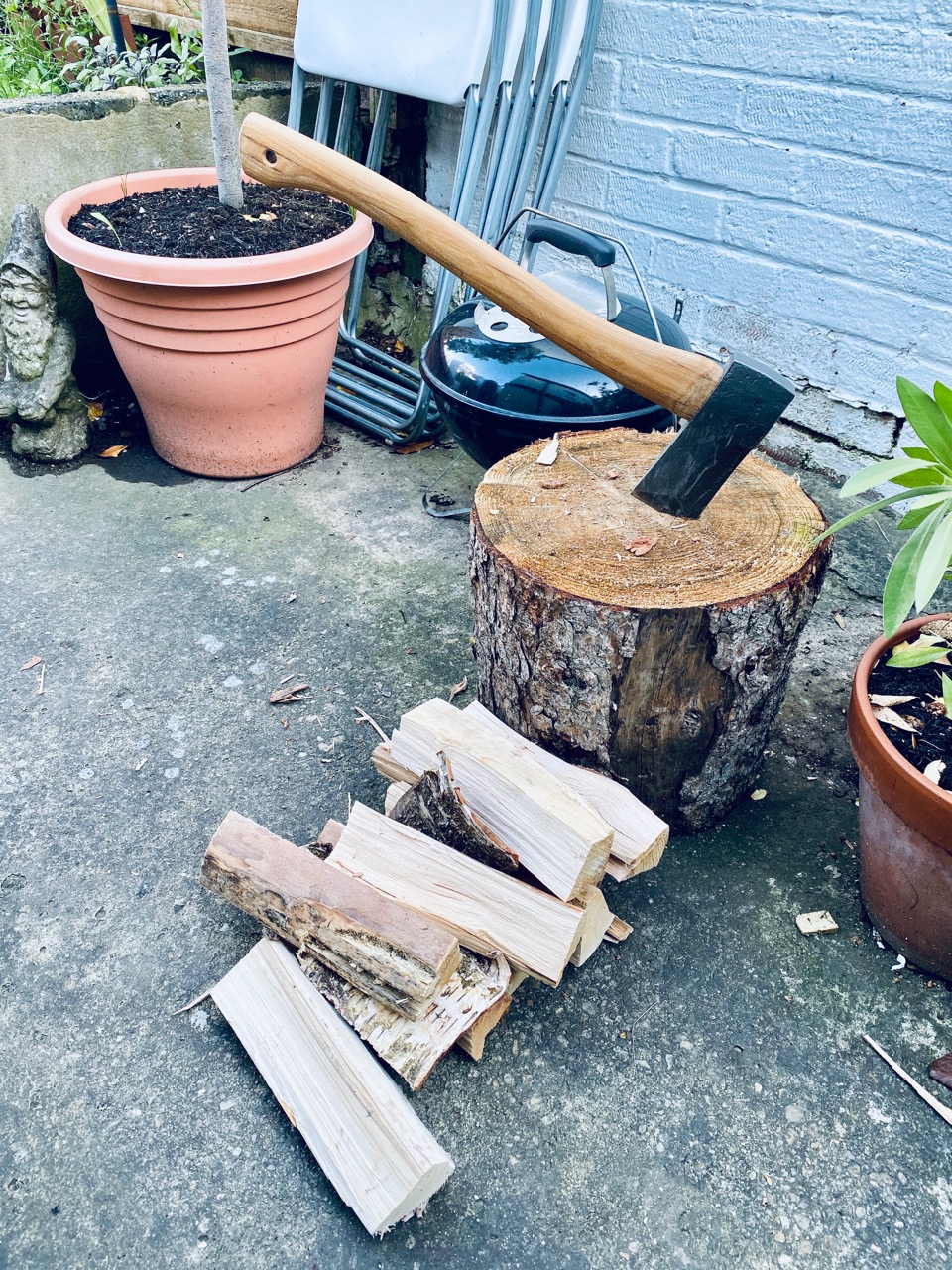 Pile of wood next to a chopping block with an axe in it